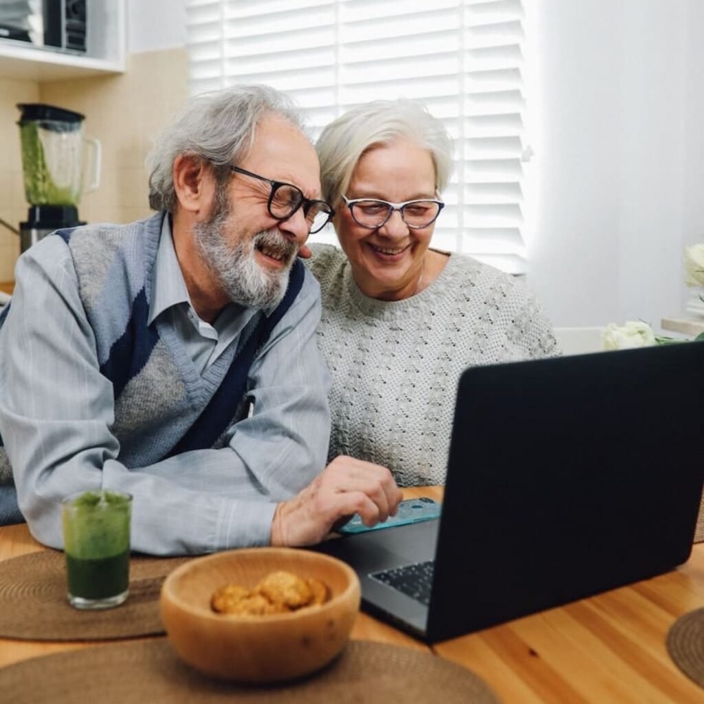 An older couple smiling at a laptop at their kitchen table